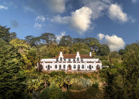 Long, two story white house set amid greenery on a hillside.