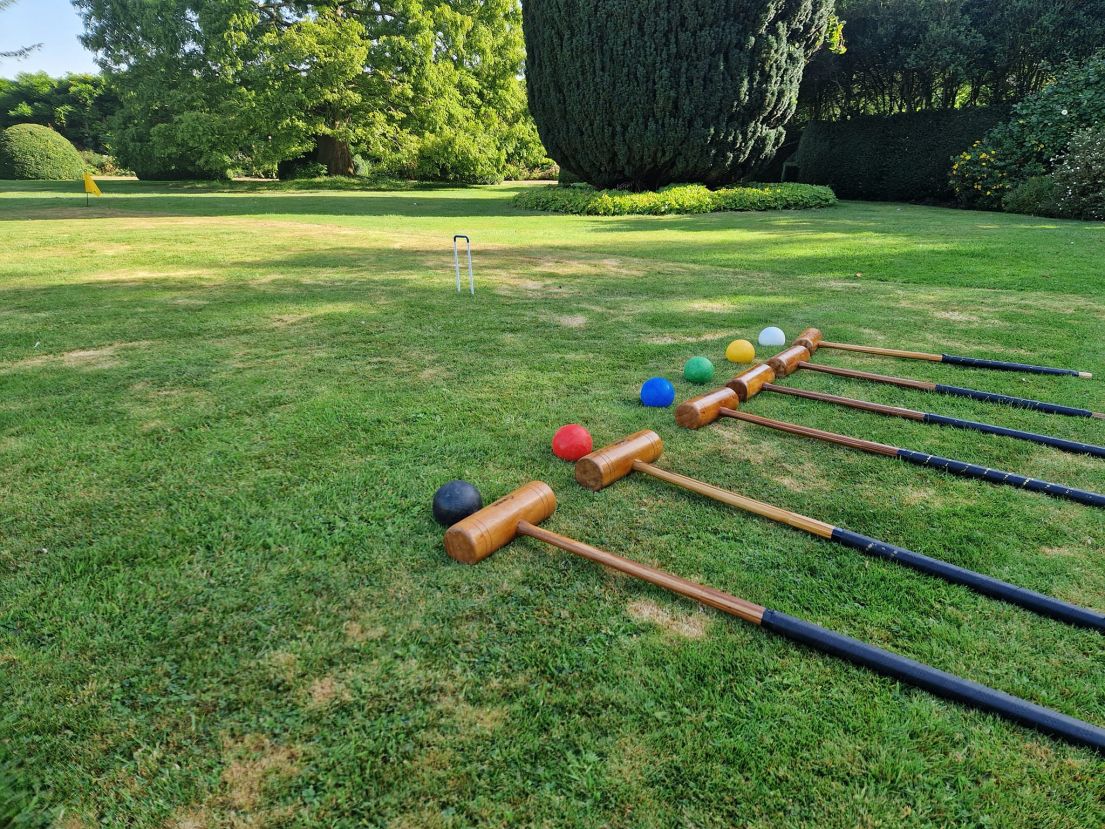 Six croquet mallets and their coloured balls laid down on a green lawn.