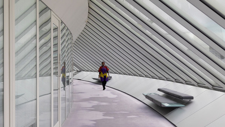 Woman walking down a curved white corridor in a modern building with angled ceiling and glass wall.