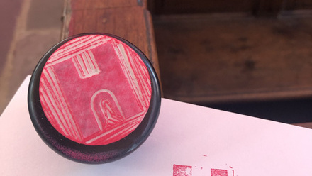 Pink H inked stamp and its print on a piece of white paper.
