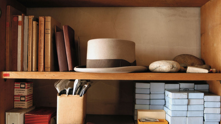 Elegant grey hat with black band sat in the middle of a set of shelves.