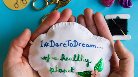 Embroidered fabric cloud cupped in two hands against a blue background.