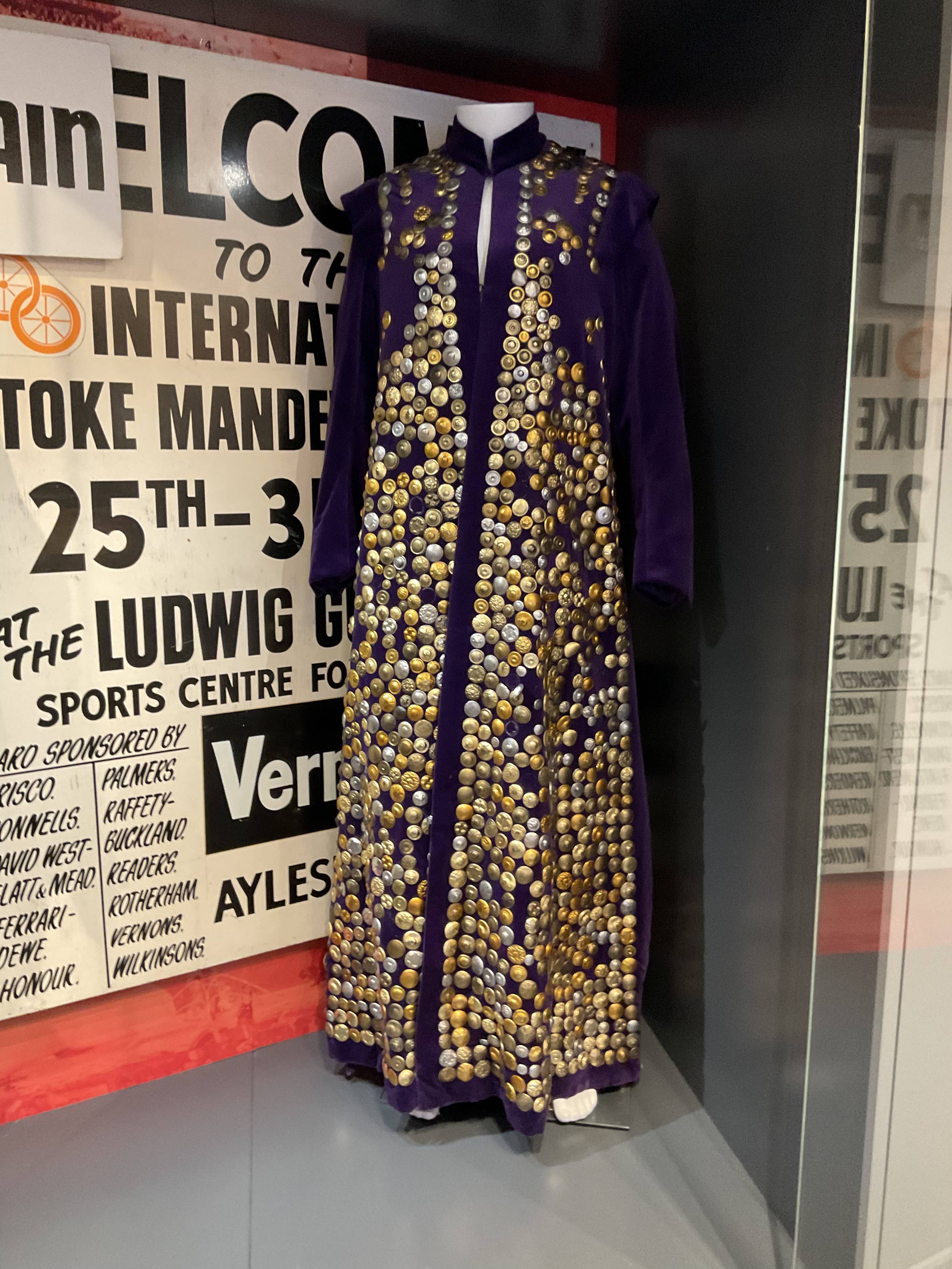 Museum display of a purple velvet cloak covered with round metallic discs.