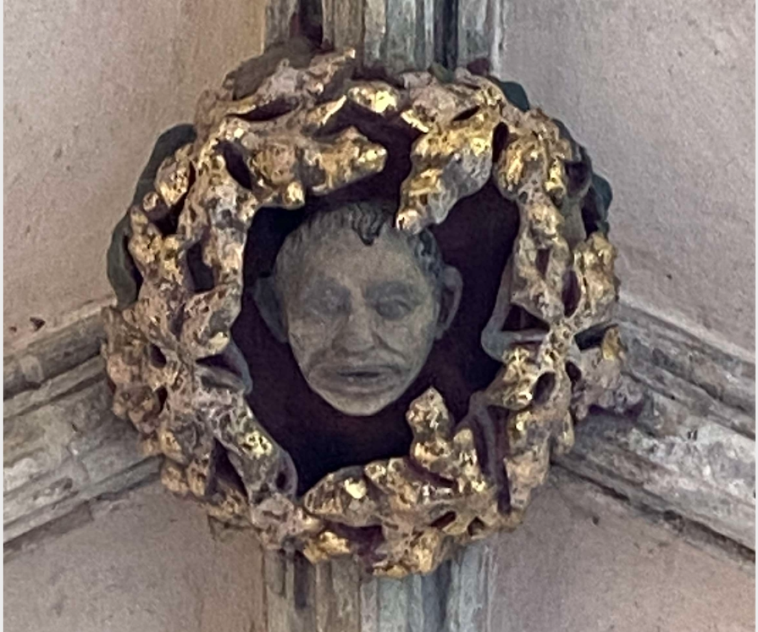 A close up of a grey carving of a man's face, framed by gold foiled stone on a stone ceiling.