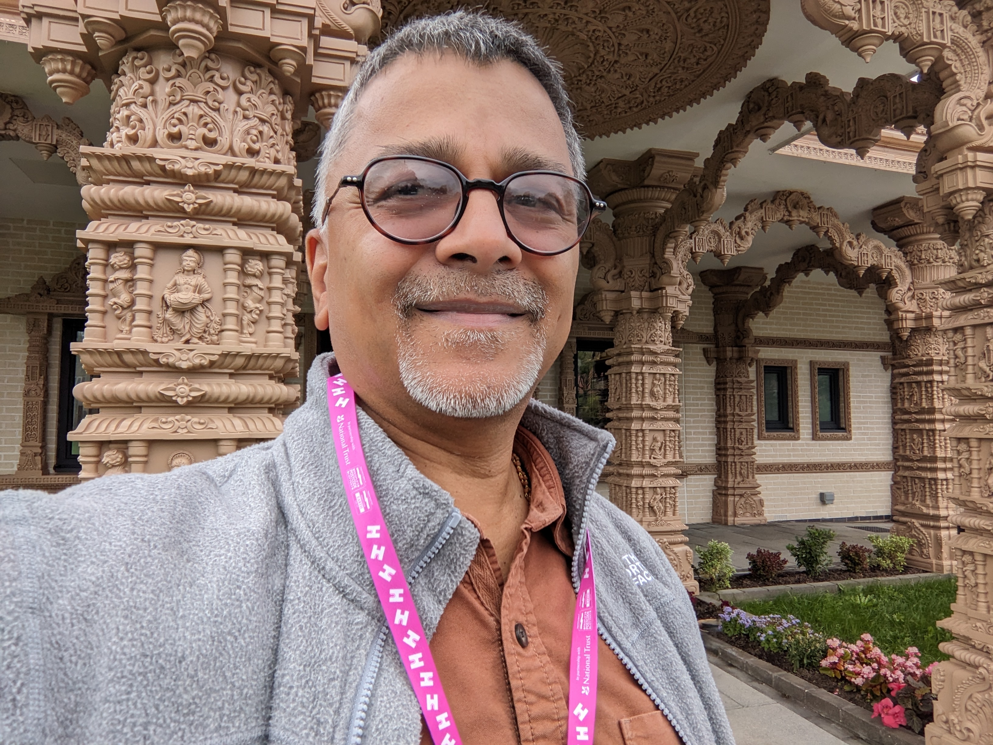 Man wearing glasses and a pink lanyard in front of ornate colonnade 