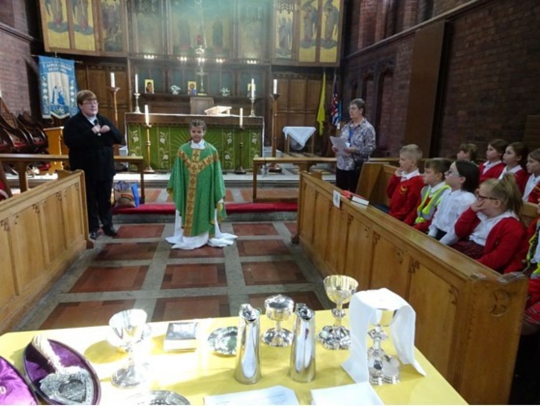 Children watching on as another small boy dressed in green church robes, demonstrates the traditional robes and table of church chalices. 