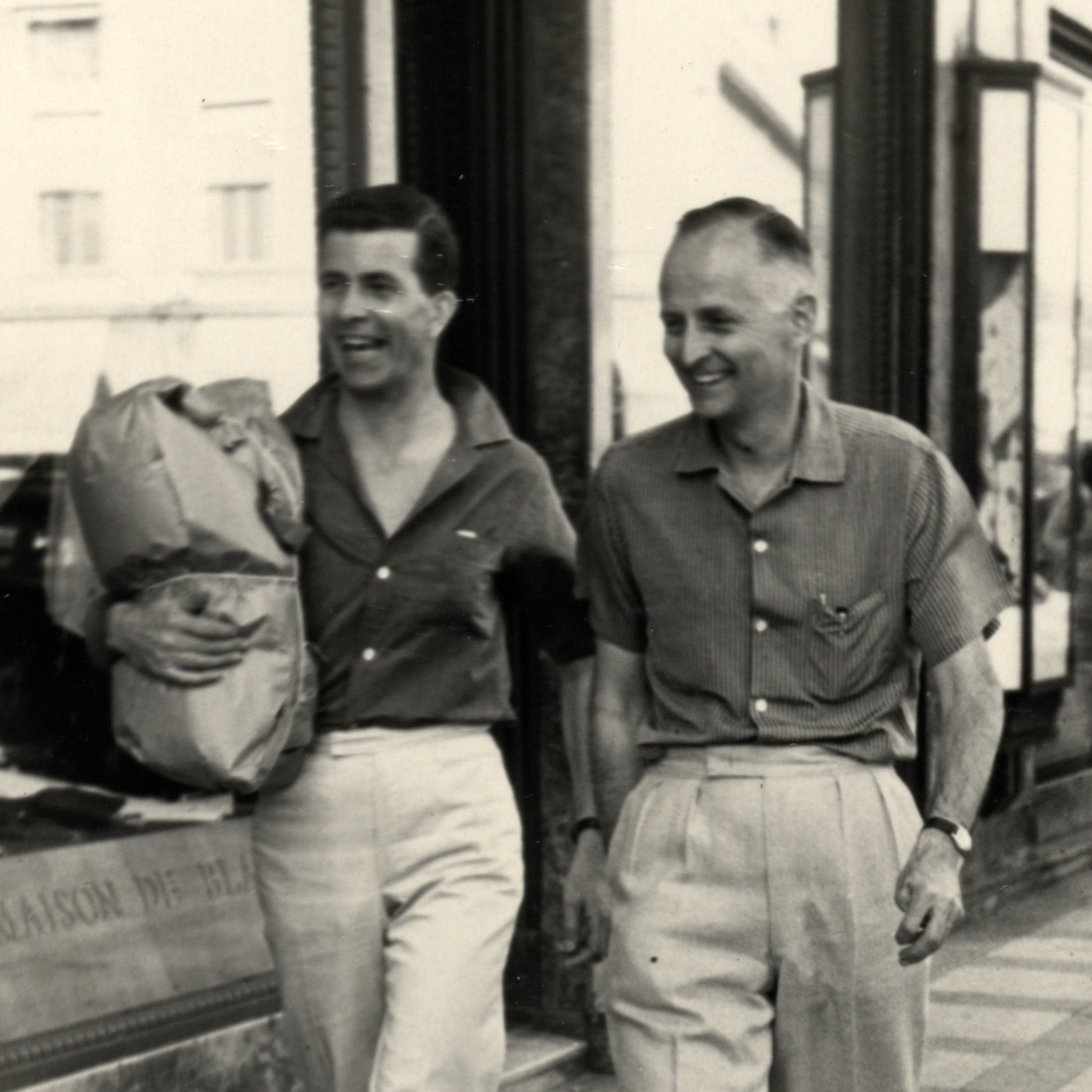 Old photograph of two men walking down a street, smiling.