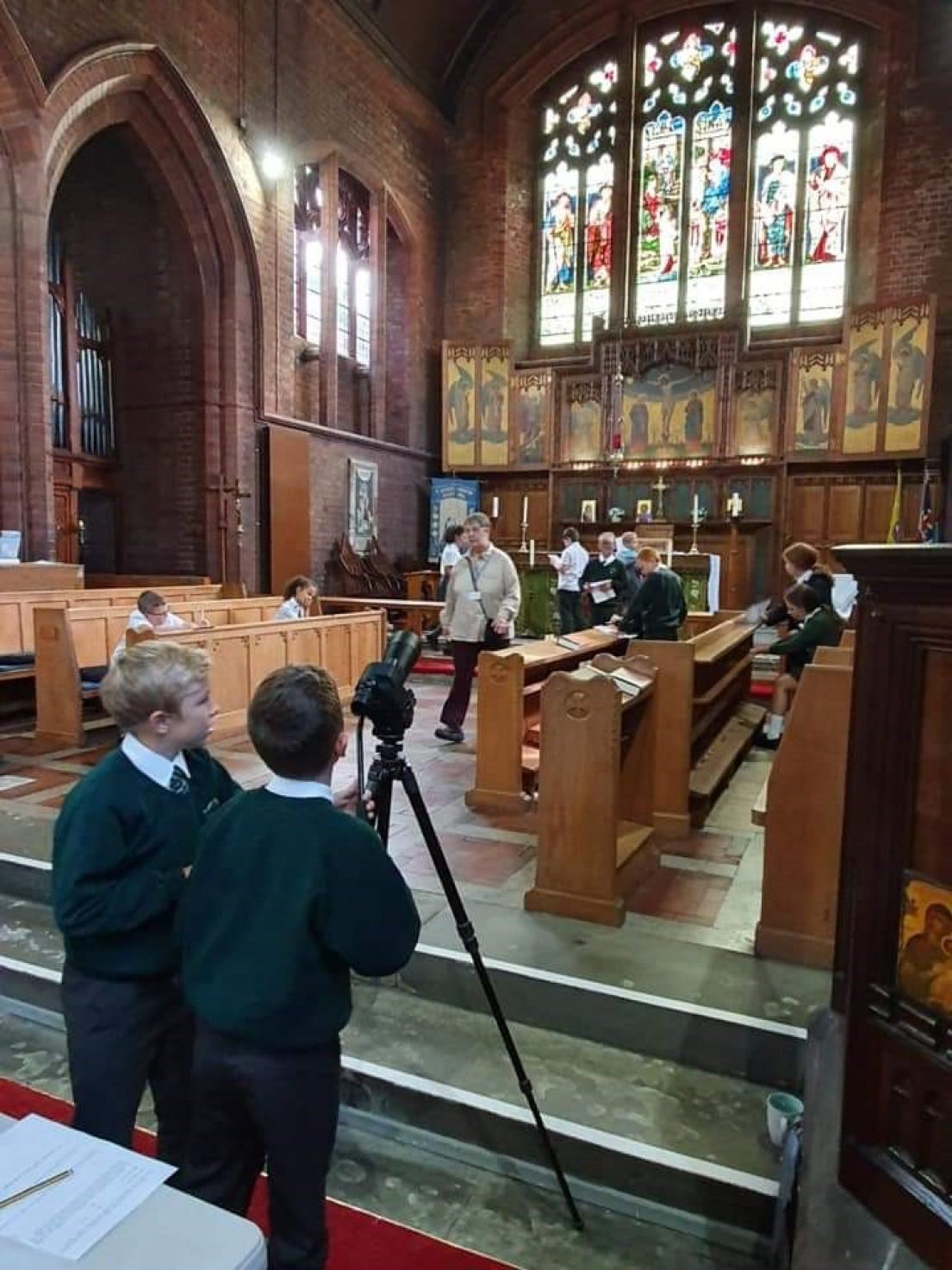 Primary school children using telescopes to look closer at the stained glass window showing the dragon in the chalice. Other children are exploring.