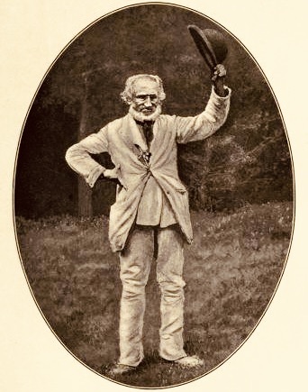 Sepia oval shaped photograph of older man with white beard standing in a garden in a pale suit, hand on hip and waving a bowler hat
