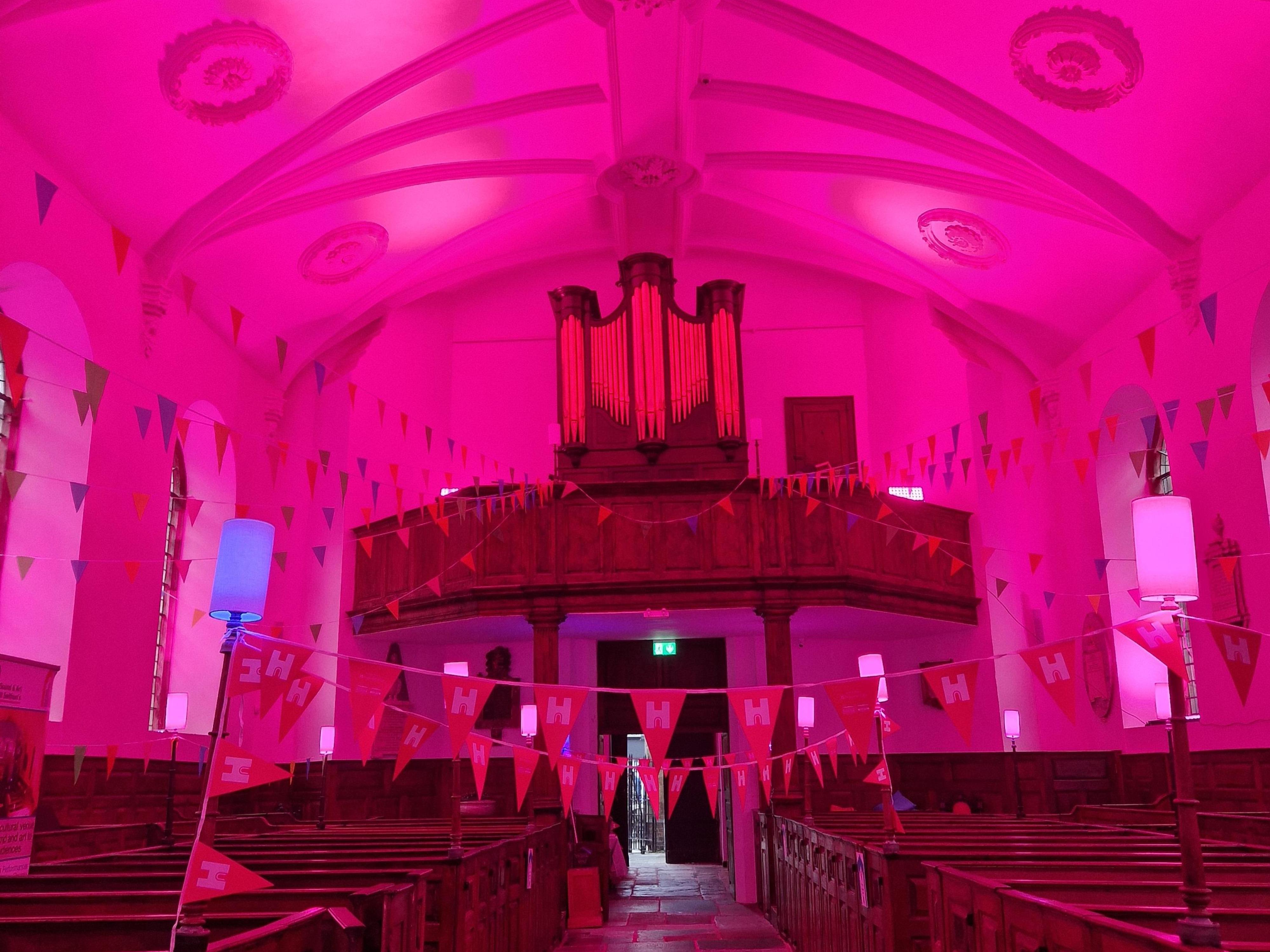 Church interior with wooden pews and plasterwork ceiling - lit in a strong pink colour.