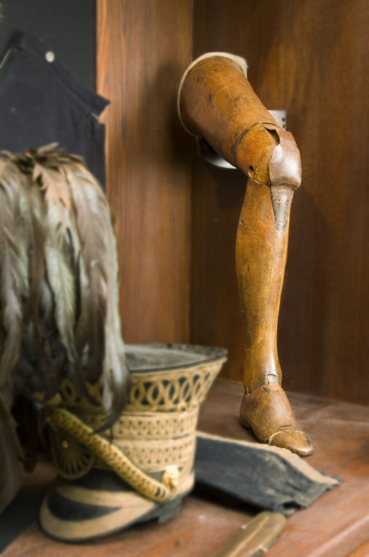 Articulated wooden leg leans against a corner beside a plumed helmet.