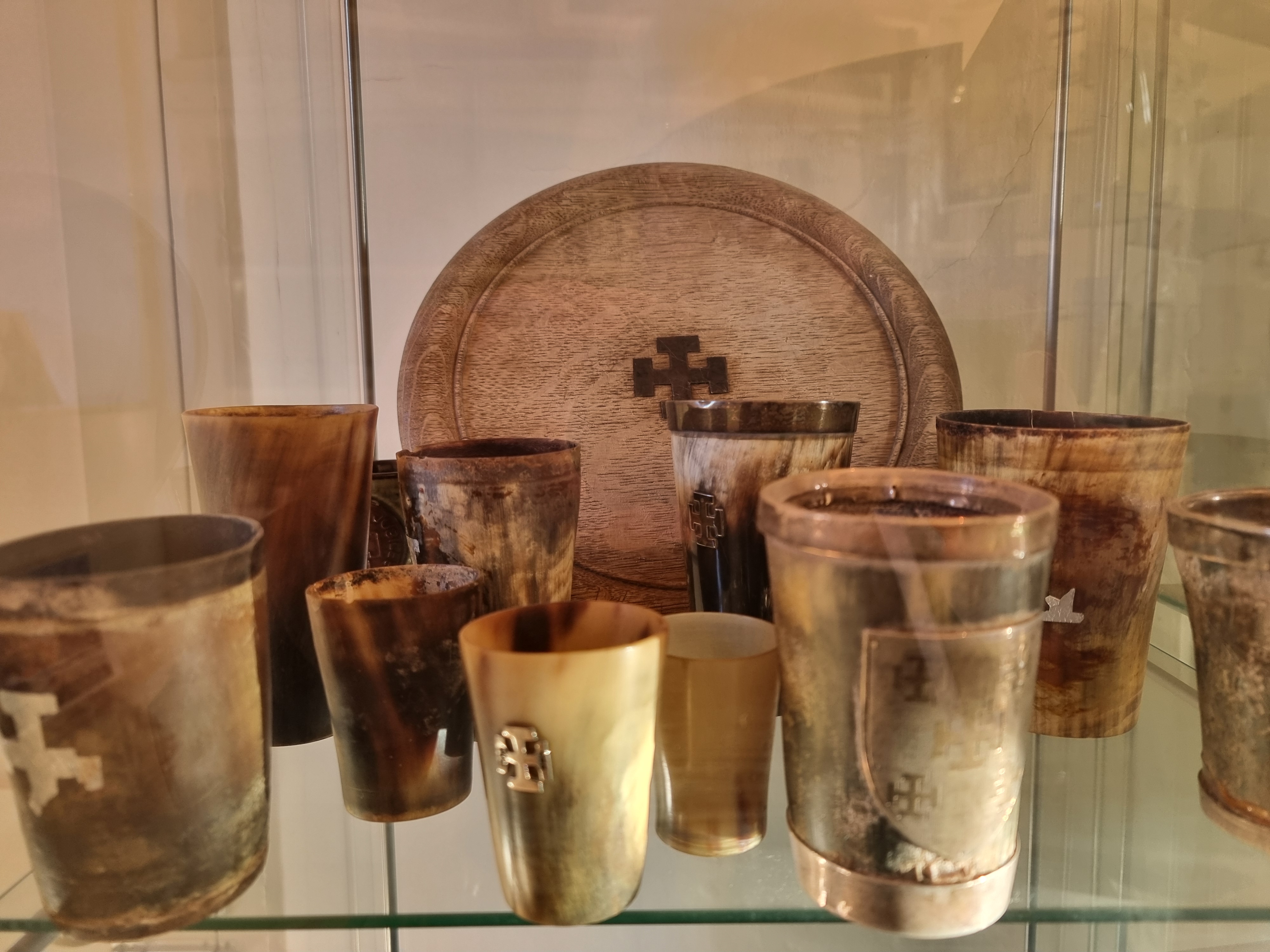 Small plate and several horn beaker style cups on a glass shelf.