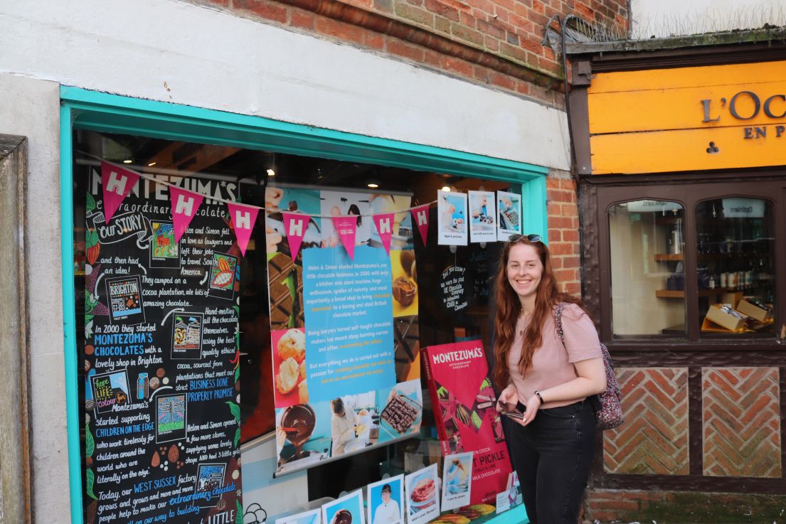 A lady with long auburn hair, pink top and black jeans, standing outside a shop window adorned with 'HODs' bunting. 