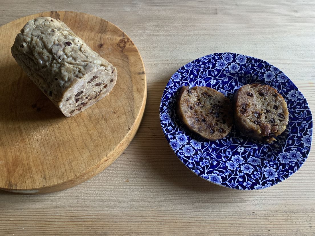 A cylindrical beige pudding with visible currents. There are two round slices placed on a blue flower plate