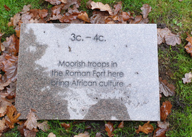 Rectangular stone memorial slab on grass covered with autumn leaves.