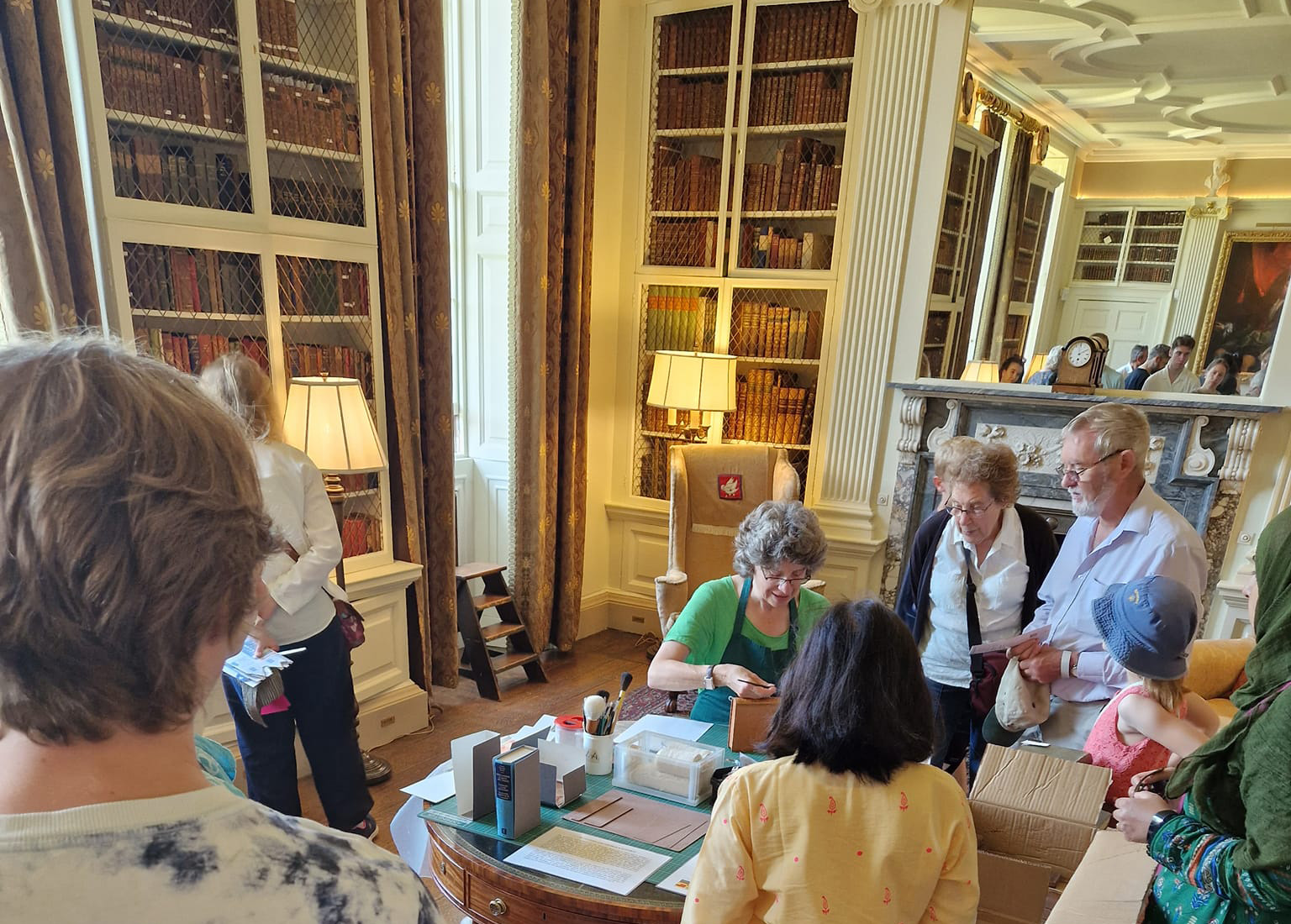 Small group of people of varying ages gathered round a small table covered with conservation equipment in the library of a historic house.